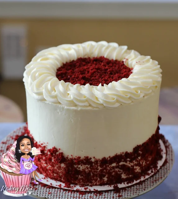 Red velvet celebration cake by Kakey Mae. White piped swirls and red cake crumbs around a tall celebration cake.