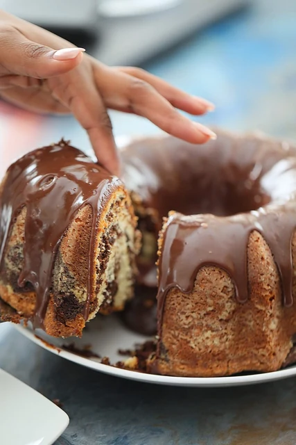 Chocolate-glazed marble Bundt by Kakey Mae. A chocolate-glazed Bundt cake with a slice lifted to show its marbled center.