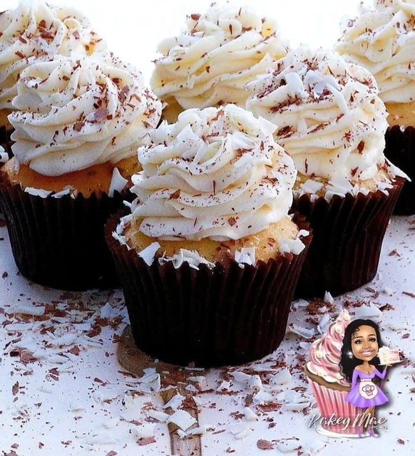 Coconut-topped cupcakes by Kakey Mae. Tall white frosting swirls finished with coconut and chocolate shavings.