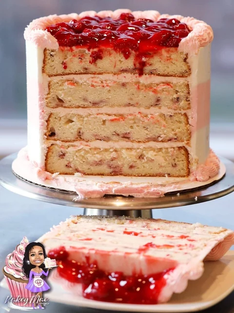 Berry layers inside by Kakey Mae. A sliced celebration cake with pale layers, a pink finish, and a glossy red fruit topping.