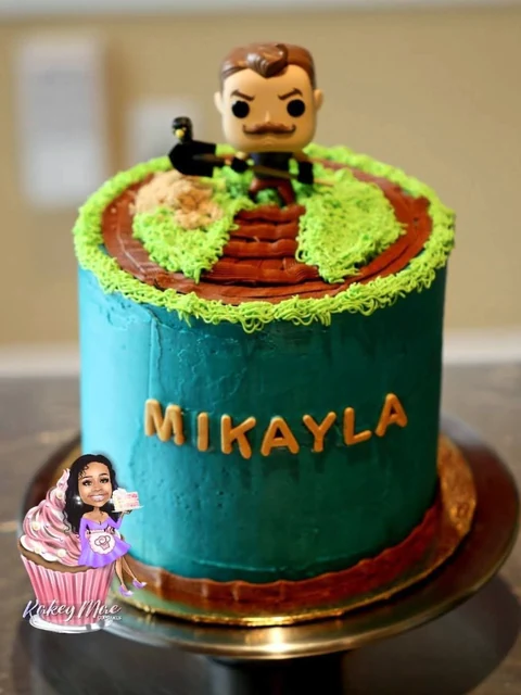 Character adventure cake by Kakey Mae. A teal cake with a grassy top, a character figure, and a personalized name.