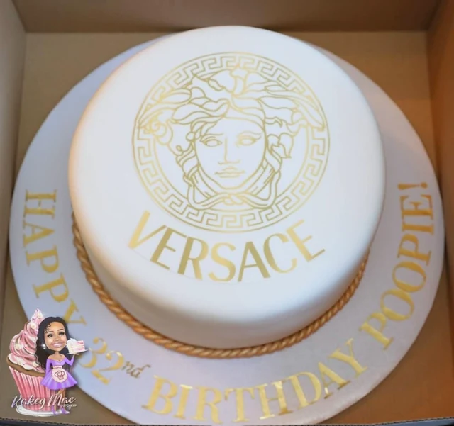 Gold fashion-inspired birthday cake by Kakey Mae. A white-and-gold cake with a detailed fashion-inspired emblem and a personalized cake board.