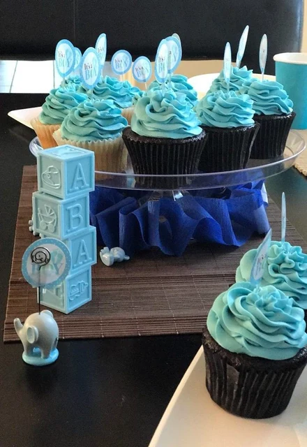 Blue celebration cupcakes by Kakey Mae. Blue buttercream swirls, coordinated decorations, and upright toppers.