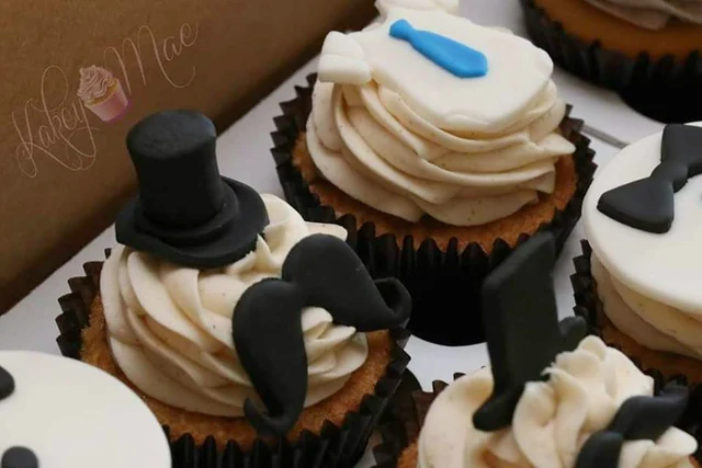 Top hat & mustache details by Kakey Mae. Black top hats and mustaches with blue tie accents on buttercream cupcakes.