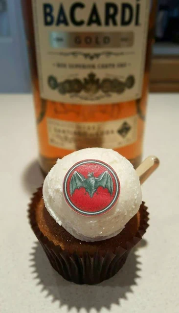 Spirit-inspired party cupcake by Kakey Mae. A cupcake with a personalized round topper, presented alongside a rum bottle.